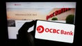 Person holding smartphone with logo of Oversea-Chinese Banking Corporation (OCBC Bank) on screen in front of website. Royalty Free Stock Photo