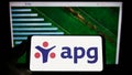 Person holding smartphone with logo of pension fund Algemene Pensioen Groep (APG) on screen in front of website.