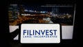 Person holding smartphone with logo of real estate company Filinvest Land Inc. (FLI) on screen in front of website.