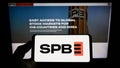 Person holding smartphone with logo of Russian financial marketplace SPB Exchange on screen in front of website.