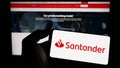 Person holding smartphone with logo of Spanish banking company Banco Santander S.A. on screen in front of website.