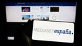 Person holding smartphone with logo of Spanish media company Mediaset Espana on screen in front of website.