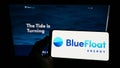 Person holding smartphone with logo of Spanish renewables company BlueFloat Energy LLC on screen in front of website.