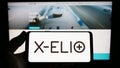 Person holding smartphone with logo of Spanish renewables company X-ELIO Energy S.L. on screen in front of website.