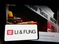 Person holding smartphone with logo of supply chain management company Li Fung Limited on screen in front of website.