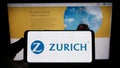 Person holding smartphone with logo of Swiss financial company Zurich Insurance Group AG on screen in front of website.