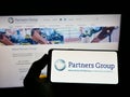 Person holding smartphone with logo of Swiss investment company Partners Group Holding AG on screen in front of website.