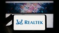 Person holding smartphone with logo of Taiwanese company Realtek Semiconductor Corp. on screen in front of website. Royalty Free Stock Photo