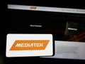 Person holding smartphone with logo of Taiwanese semiconductor company MediaTek Inc. on screen in front of website.