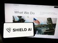 Person holding smartphone with logo of US aerospace and defense company Shield AI on screen in front of website.