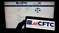 Person holding smartphone with logo of US Commodity Futures Trading Commission (CFTC) on screen in front of website.