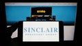 Person holding smartphone with logo of US company Sinclair Broadcast Group Inc. (SBG) on screen in front of website.