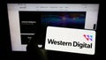 Person holding smartphone with logo of US company Western Digital Corporation (WDC) on screen in front of website.