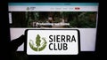 Person holding smartphone with logo of US environmental organization Sierra Club on screen in front of website.