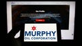 Person holding smartphone with logo of US exploration company Murphy Oil Corporation on screen in front of website.