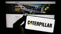 Person holding smartphone with logo of US heavy equipment company Caterpillar Inc. on screen in front of website.