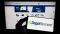 Person holding smartphone with logo of US motor company Regal Rexnord Corporation on screen in front of website.