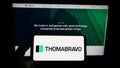 Person holding smartphone with logo of US private equity company Thoma Bravo L.P. on screen in front of website.