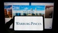 Person holding smartphone with logo of US private equity company Warburg Pincus LLC on screen in front of website.
