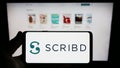 Person holding smartphone with logo of US publishing platform company Scribd Inc. on screen in front of website.
