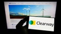 Person holding smartphone with logo of US renewables company Clearway Energy Inc. on screen in front of website.