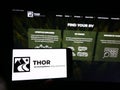 Person holding smartphone with logo of US RV manufacturing company Thor Industries Inc. on screen in front of website.