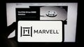 Person holding smartphone with logo of US semicondurctor company Marvell Technology Inc. on screen in front of website. Royalty Free Stock Photo