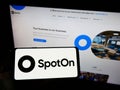 Person holding smartphone with logo of US software company SpotOn Transact LLC on screen in front of website.