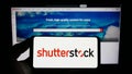 Person holding smartphone with logo of US stock photography company Shutterstock Inc. on screen in front of website.