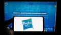 Person holding smartphone with logo of US toys and entertainment company Hasbro Inc. on screen in front of website.