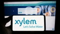 Person holding smartphone with logo of US water technology company Xylem Inc. on screen in front of website.