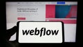Person holding smartphone with logo of US web development software company Webflow Inc. on screen in front of website. Royalty Free Stock Photo
