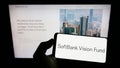 Person holding smartphone with logo of venture capital fund SoftBank Vision Fund on screen in front of website.