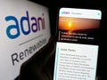 Person holding smartphone with webpage of Indian company Adani Green Energy Limited on screen in front of logo.