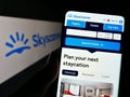 Person holding smartphone with webpage of travel metasearch company Skyscanner Ltd. on screen in front of logo.