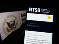Person holding smartphone with webpage of US National Transportation Safety Board (NTSB) on screen in front of seal.