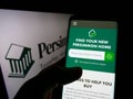 Person holding smartphone with website of British housebuilding company Persimmon plc on screen in front of logo.