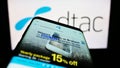 Smartphone with webpage of Total Access Communication Public Company Limited (DTAC) on screen in front of logo.