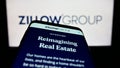 Smartphone with webpage of US real estate company Zillow Group Inc. on screen in front of business logo.