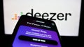 Smartphone with website of French music streaming company Deezer S.A. on screen in front of business logo.