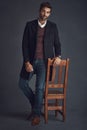 Style comes easy to him. Studio portrait of a stylishly dressed young man standing next to a chair against a gray Royalty Free Stock Photo