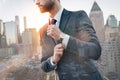 Always in style. Fashionable businessman adjusting sleeve while standing outdoors with cityscape on the background