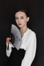 Beautiful young woman in a white Asian suit on a black background. The style of a modern geisha in the studio.