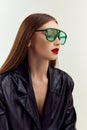 Style. Young beutiful brunnette girl posing in green suglasses and black leather jacket posing over grey studio Royalty Free Stock Photo