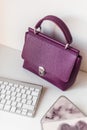 Styled violet lifestyle fashion leather bag surrounded by apple keyboard and lux stationery on minimal white background