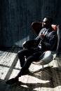 Stylish african american businessman in formal suit sits on a chair in a dark office Royalty Free Stock Photo