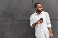 Stylish african american businessman standing in white shirt, holding a cup of coffee, having a break after online work Royalty Free Stock Photo