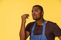Stylish African American cook wearing blue apron sends kiss with his fingers in Italian manner, against bright yellow
