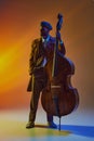Stylish African-American performer in retro casual attire holds contrabass in neon light against gradient background.