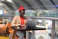 African traveler man sitting at cafe table in airport, works remotely on laptop waiting for a flight Royalty Free Stock Photo